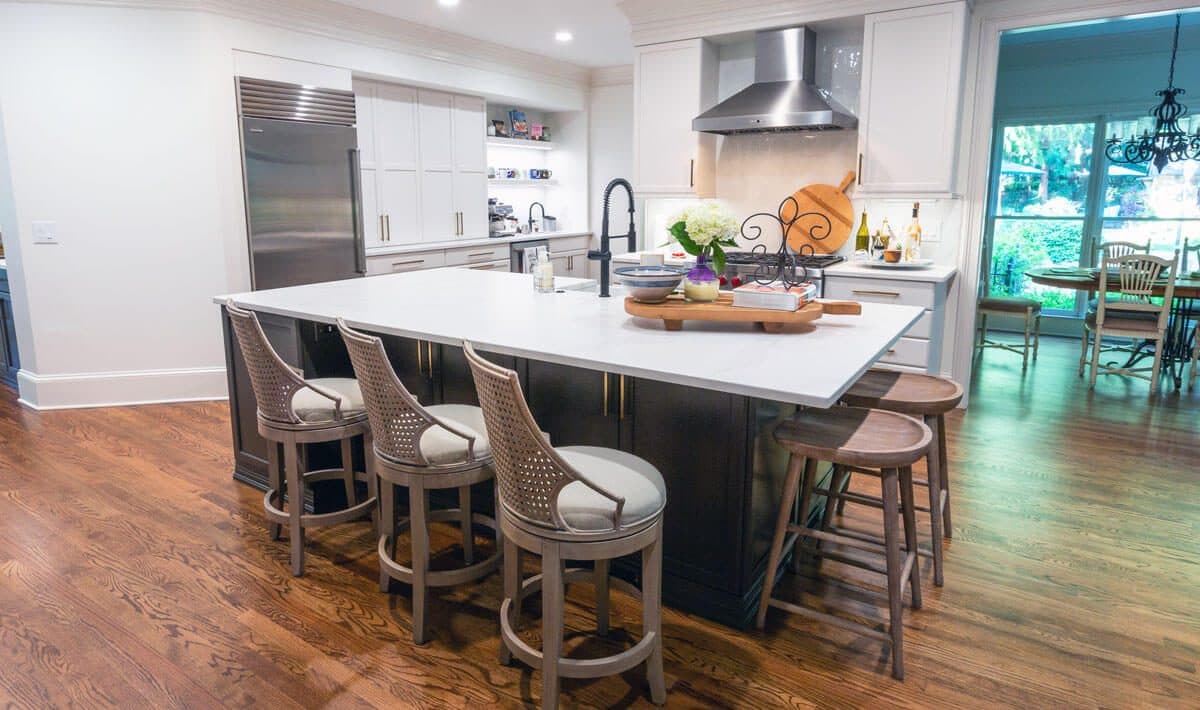 Open kitchen with a large quartz-topped island seating five, dark painted island base, white cabinetry, stainless hood and built-in refrigeration